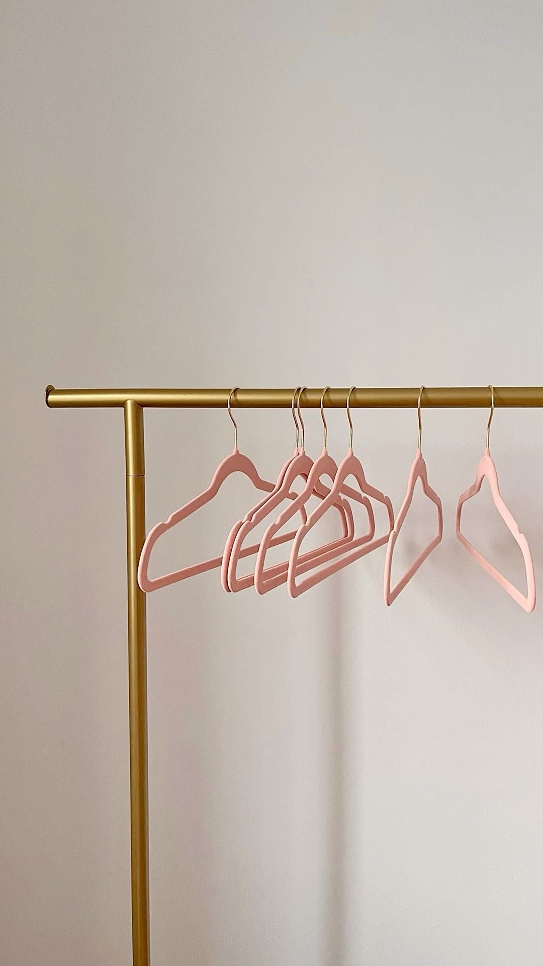 Gold clothing rack with pink hangers against a plain background